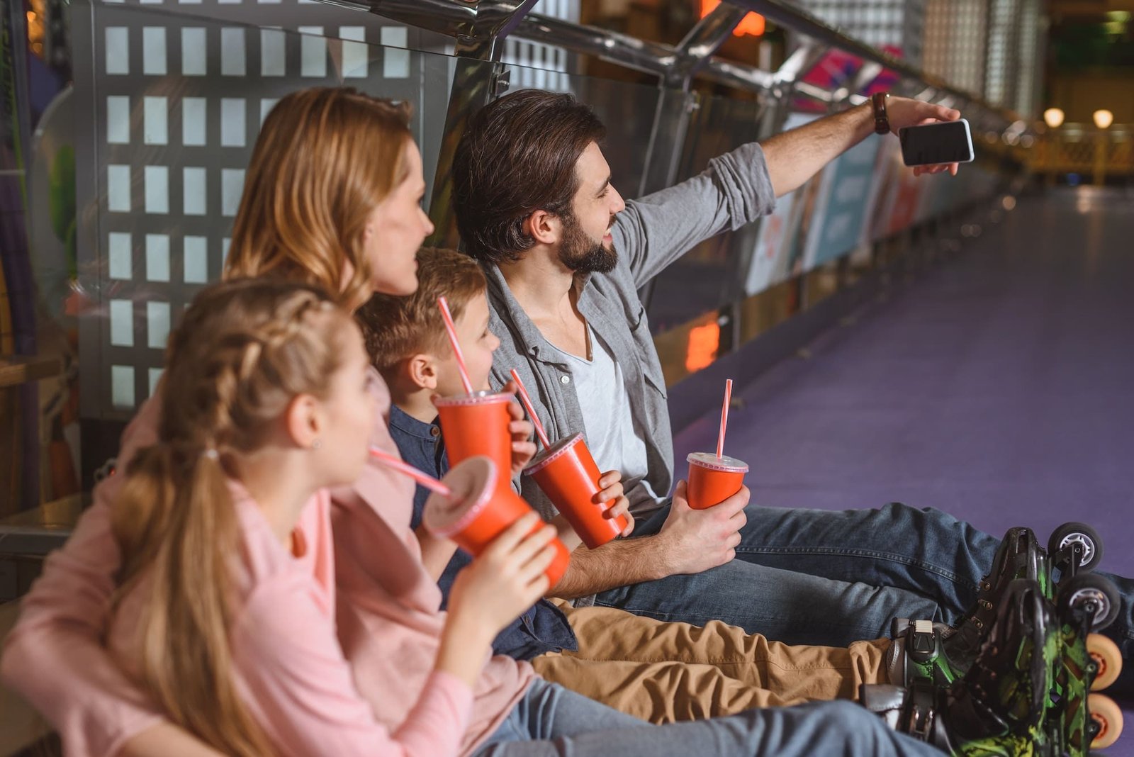 side view of family with drinks taking selfie while resting after skating on roller rink